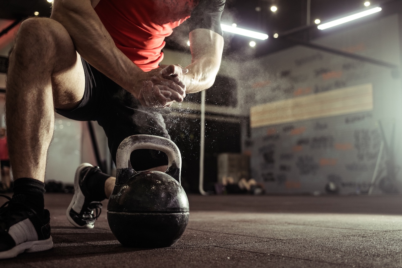 Man kneels over kettlebell with drying powder on his hands